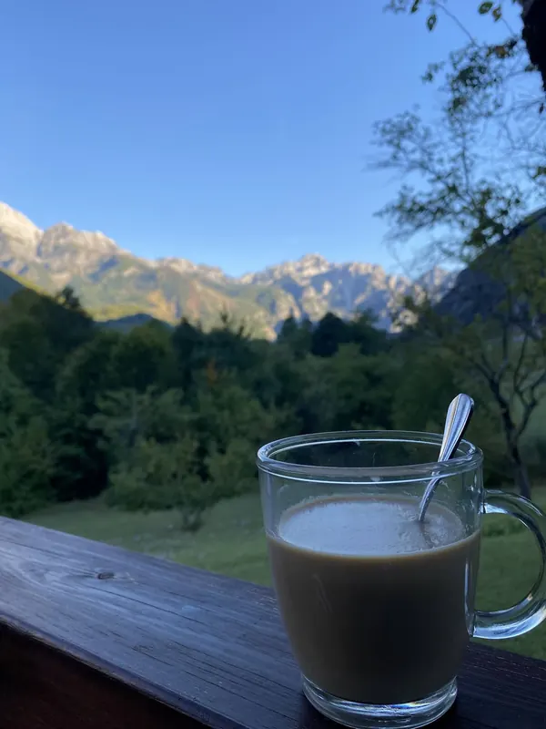 A glass of coffee on the wooden railing, peaks catching the morning light