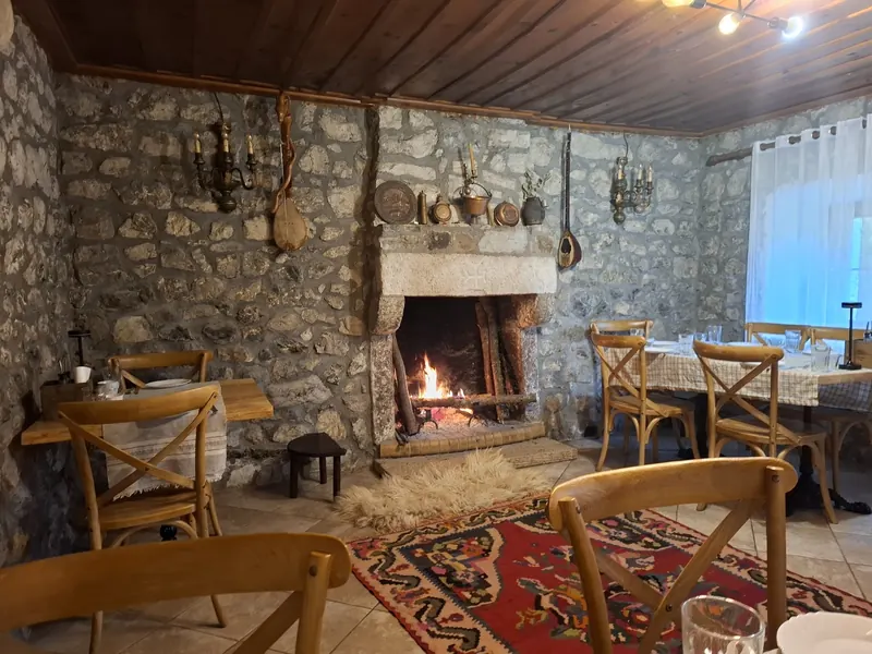 The stone dining room with an open fire, wooden chairs and a red kilim