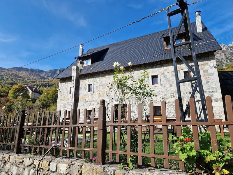 The stone guest house behind its wooden fence under a blue autumn sky